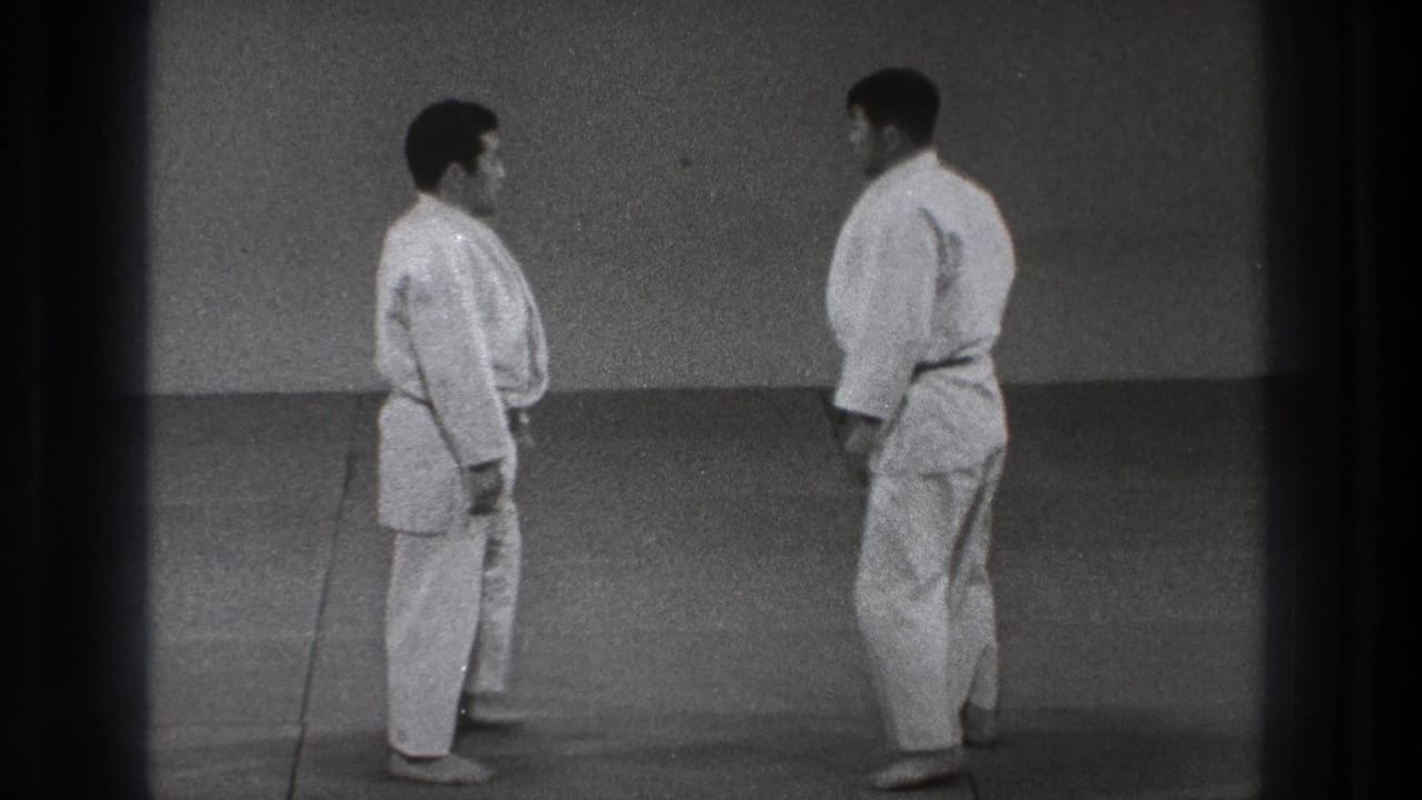 In 1971 Tokyo footage, two adult men in white gi face each other on a training mat before beginning a judo exchange.