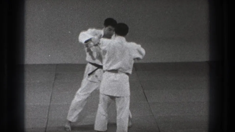 Two men in white gi move through a controlled judo technique in 1971 Tokyo archival home-movie footage.