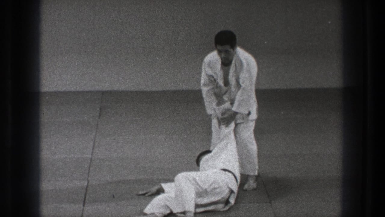After the throw, the black-belt practitioner stands over his partner and maintains arm control on the training mat.