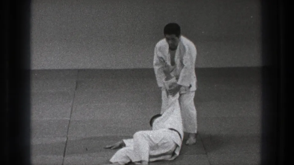 After the throw, the black-belt practitioner stands over his partner and maintains arm control on the training mat.