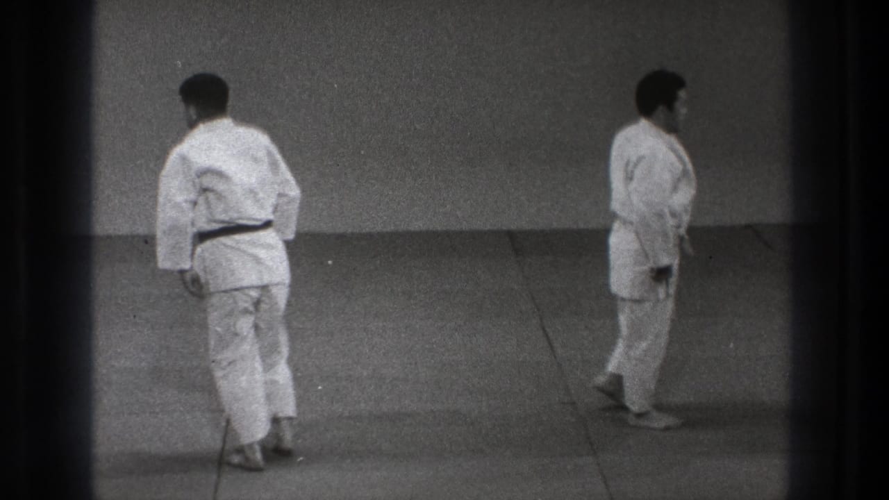 1971 Tokyo 8mm frame showing two adult men in judo uniforms separated on the mat, appearing to reset or begin walking away.