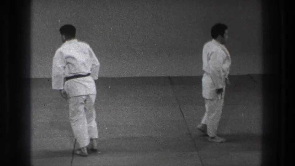 1971 Tokyo 8mm frame showing two adult men in judo uniforms separated on the mat, appearing to reset or begin walking away.