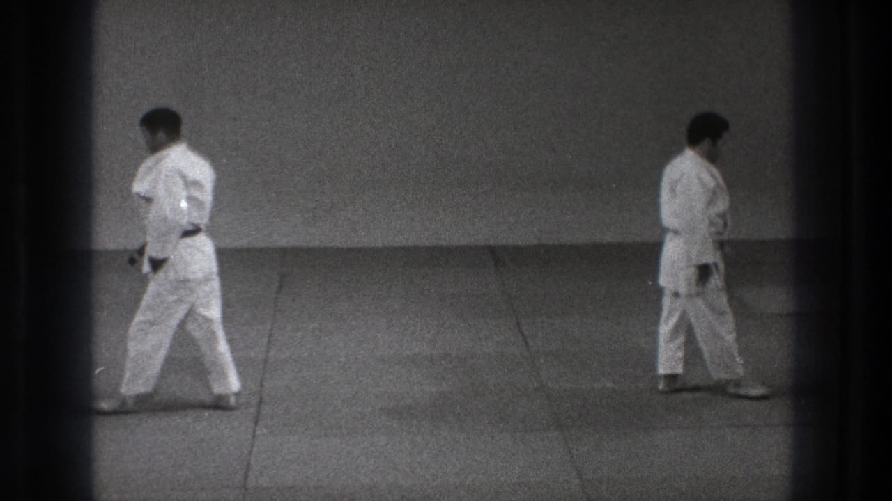 1971 Tokyo 8mm frame with two adult men in white judo uniforms walking apart across a padded mat after the practice sequence.