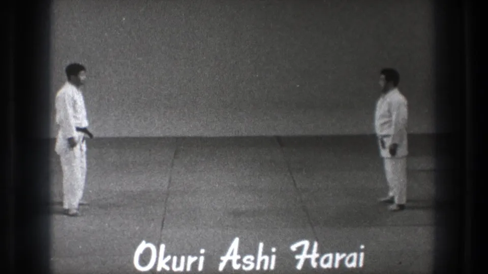 Two adult judoka face each other in the 1971 Tokyo footage as handwritten Okuri Ashi Harai text appears along the lower frame.
