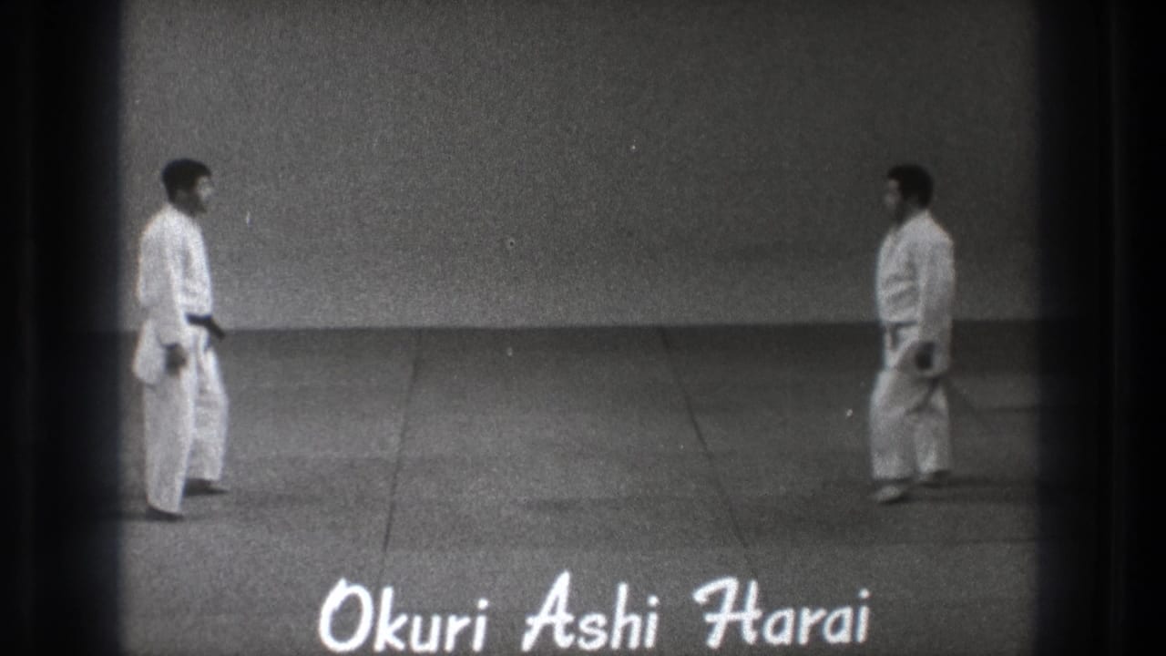 Two men in white gi face each other on a mat with handwritten title text over the frame.
