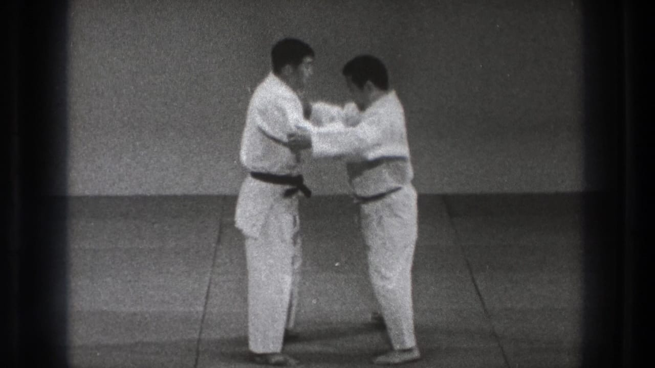 Two adult men in gi begin contact, with one practitioner holding or adjusting the other's uniform during the 1971 Tokyo dojo footage.