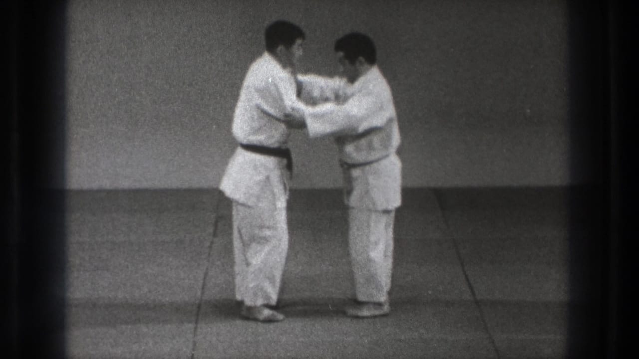 Two men in white gi face each other on a mat, holding each other's sleeves or lapels.