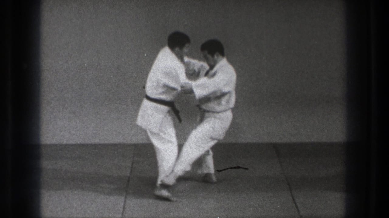 In the supported 1971 Tokyo setting, one martial artist lowers his stance while the partner controls the upper body grip.