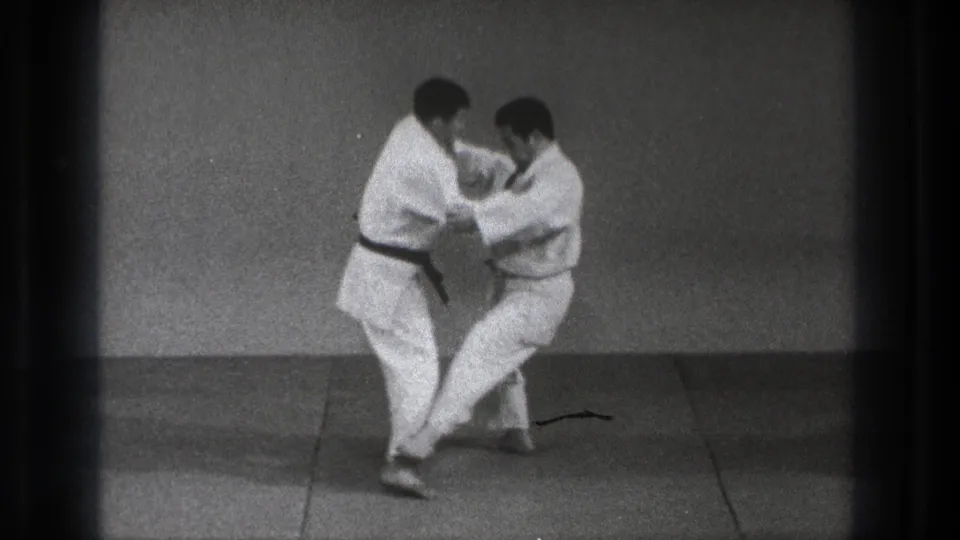 In the supported 1971 Tokyo setting, one martial artist lowers his stance while the partner controls the upper body grip.