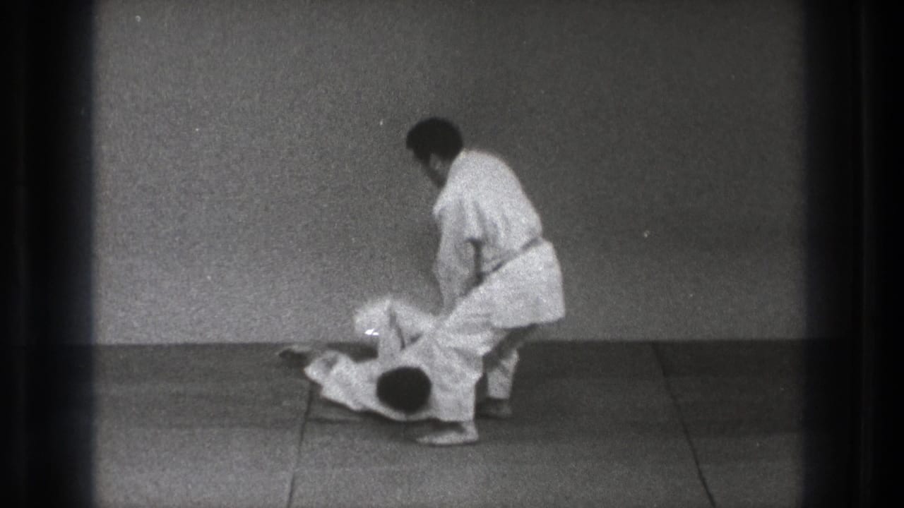 After the takedown, one man in a white gi stands while his partner lies on the mat in the Tokyo 1971 martial arts practice clip.