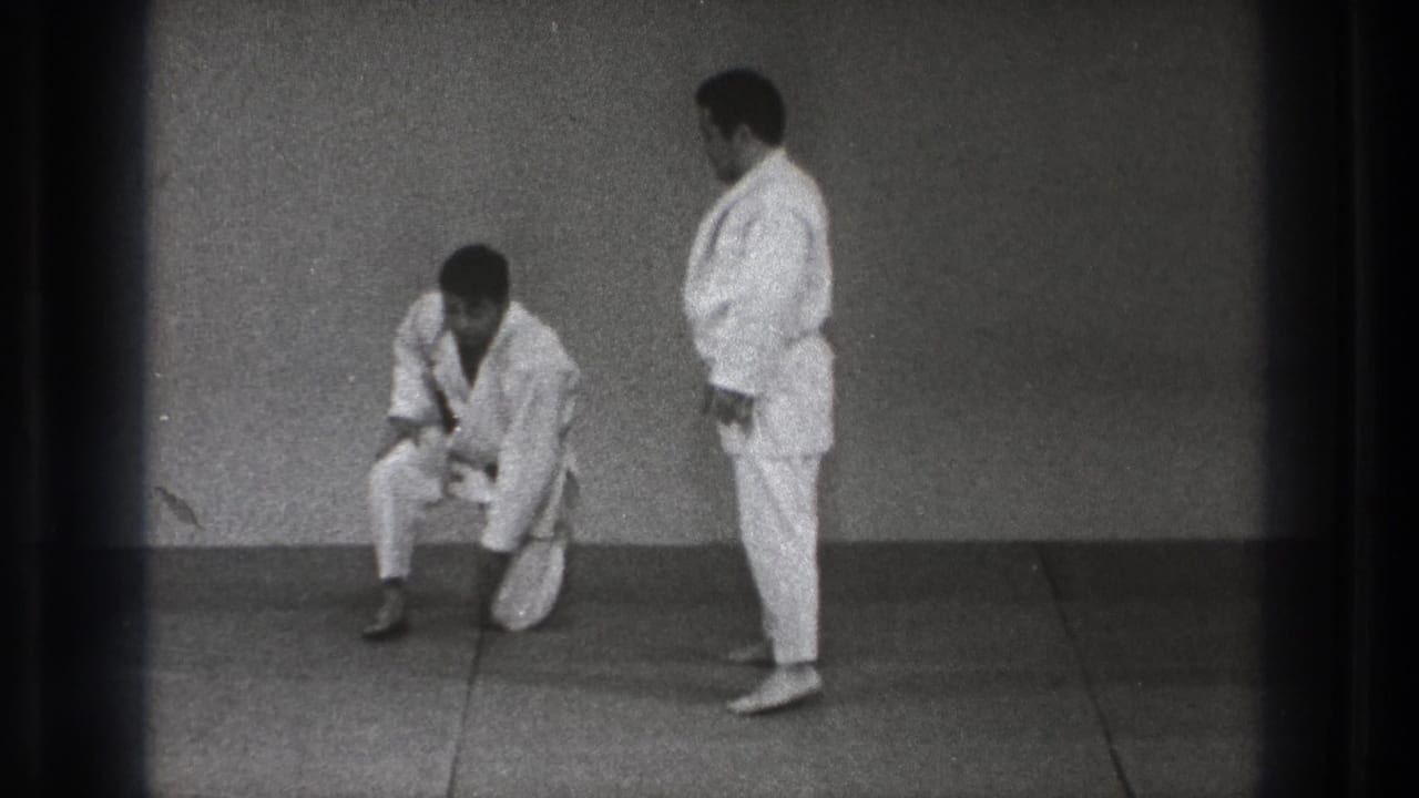 1971 Tokyo judo practice frame with one man kneeling or rising while another stands beside him in a simple dojo.