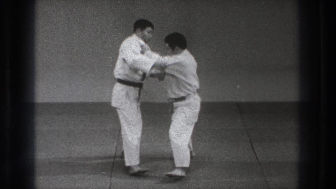 One practitioner bends his knees and lowers his stance while holding the other man's gi during the 1971 Tokyo practice sequence.