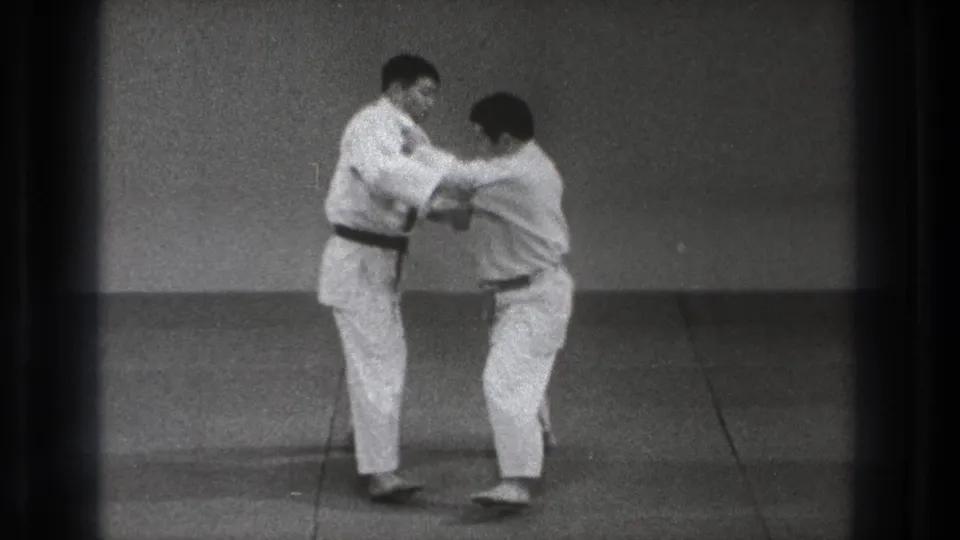 One practitioner bends his knees and lowers his stance while holding the other man's gi during the 1971 Tokyo practice sequence.