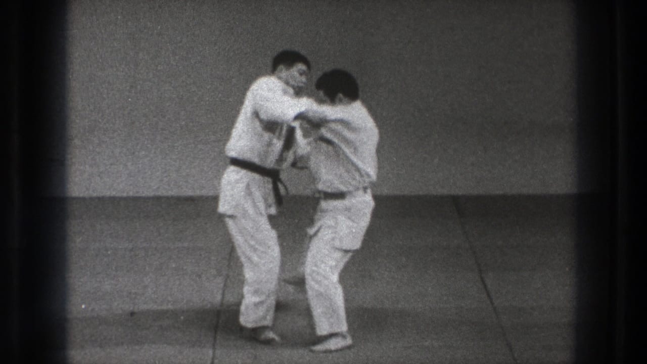 In metadata-supported 1971 Tokyo footage, two men in white martial arts uniforms begin a judo grip exchange on an indoor mat.