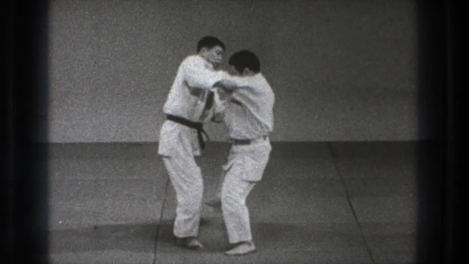 In metadata-supported 1971 Tokyo footage, two men in white martial arts uniforms begin a judo grip exchange on an indoor mat.