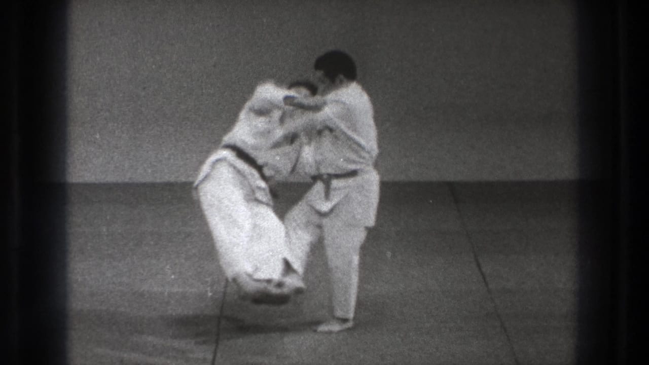 The dark-belt practitioner lifts and turns his partner during a controlled judo throw in the 1971 Tokyo home-movie scene.