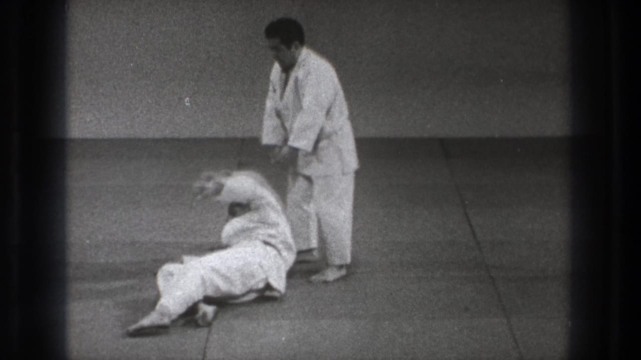 In Tokyo 1971 home-movie footage, one man in a white uniform stands as another falls or rolls on a dojo mat.