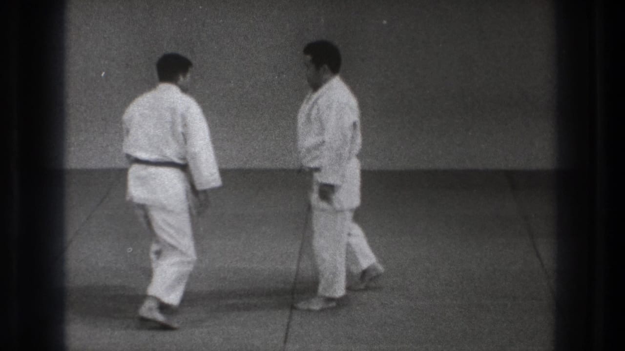 Two adult men in white martial arts uniforms reset their stance on a dojo mat in Tokyo 1971 footage.