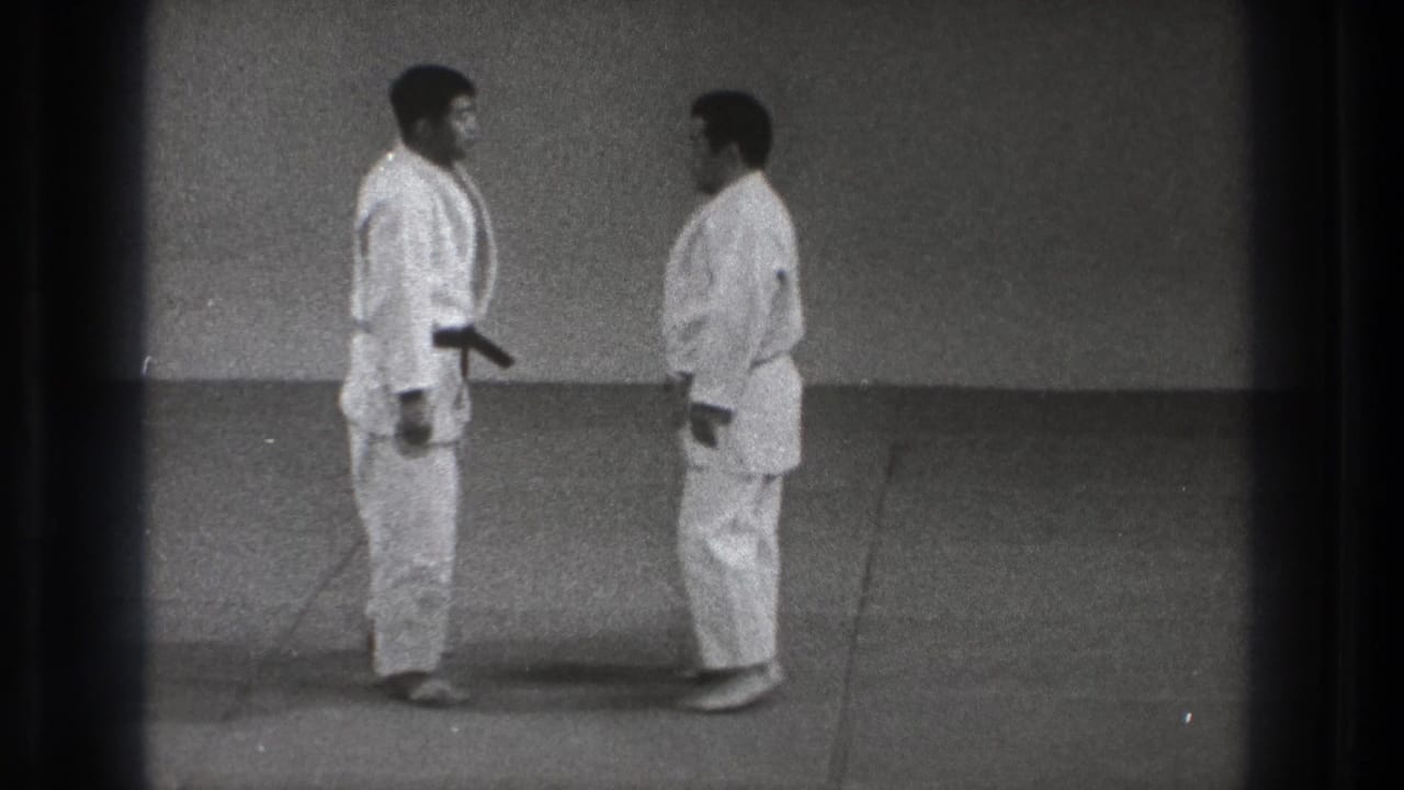 The two men stand face to face in a simple dojo, their white uniforms and mat floor visible in the 1971 Tokyo clip.