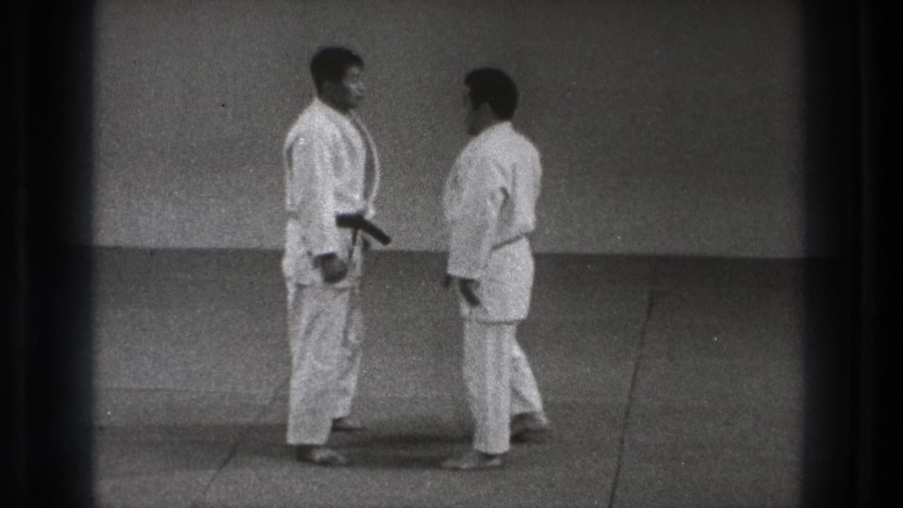 Two men in white gi and black belts face each other on a mat.