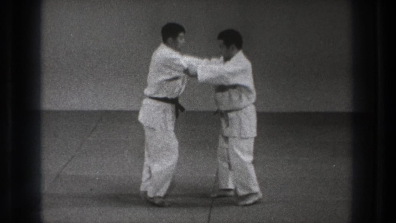 The men hold sleeve and lapel positions while facing each other in the black-and-white 8mm martial arts demonstration.