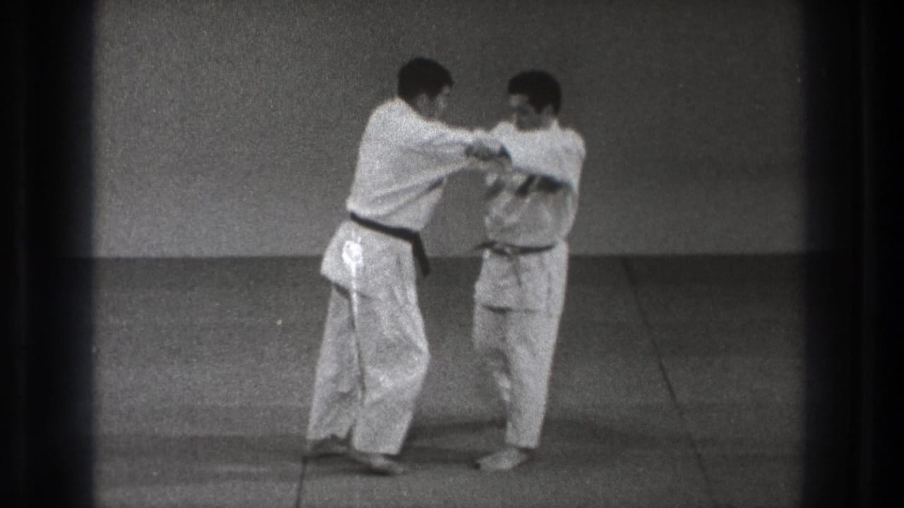 A participant steps across while holding the other man's gi, suggesting the start of the named throwing or foot-blocking technique.