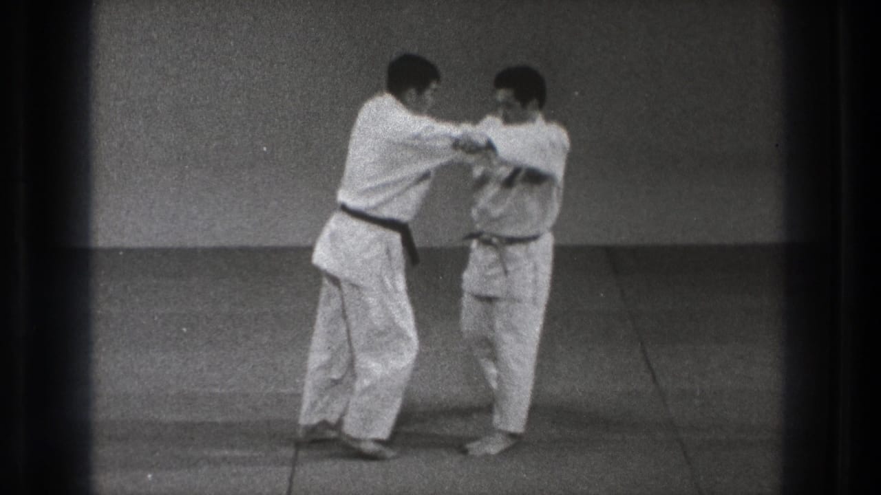 Two adult practitioners in white gi make close arm contact during a martial arts technique in the Tokyo training room.