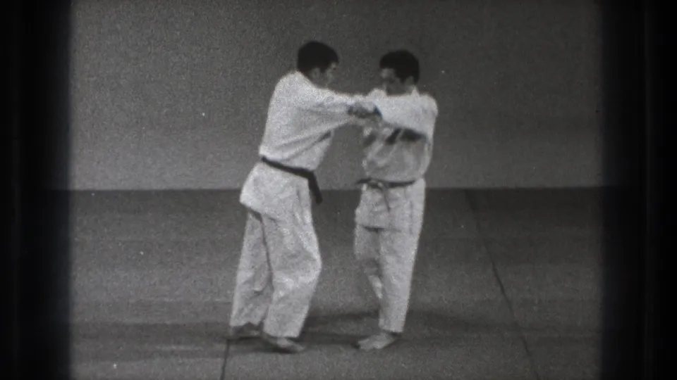 Two adult practitioners in white gi make close arm contact during a martial arts technique in the Tokyo training room.