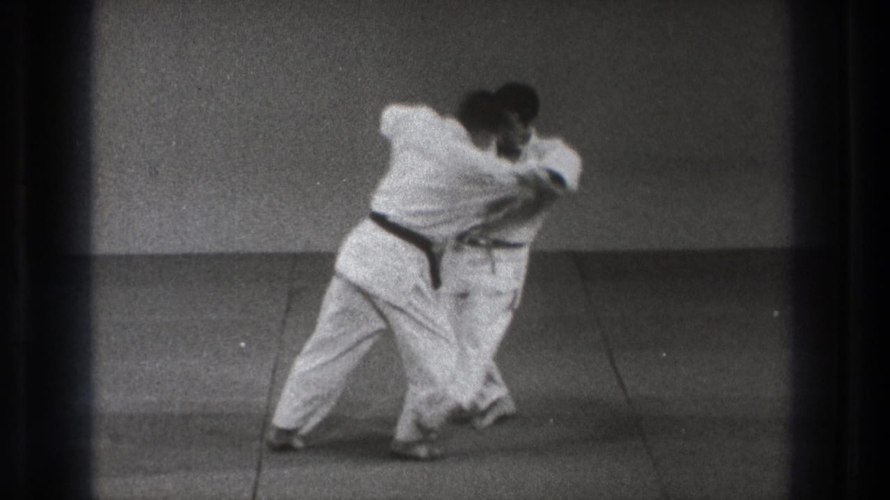 The black-belt practitioner appears to rotate into a throw as his partner bends forward on the mat.