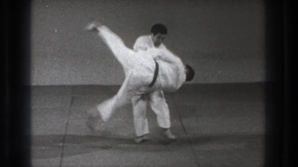 Black-and-white 8mm frame of a gi-clad martial artist completing a midair takedown in Tokyo, Japan.