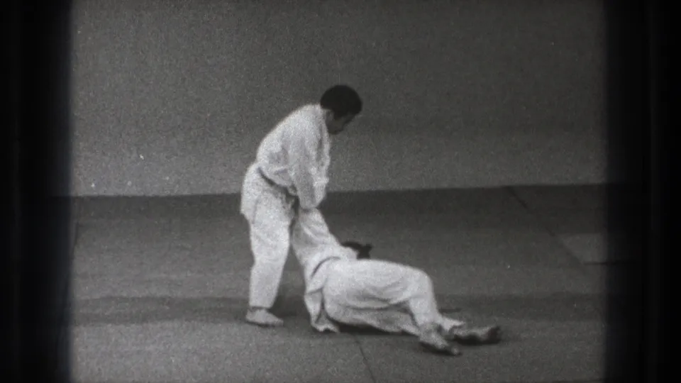 1971 Tokyo martial arts demonstration frame with one adult standing over a partner after a controlled fall.