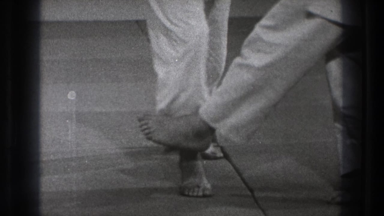 Tokyo 1971 black-and-white frame showing the end of a fall or sweep, with one practitioner low on the floor beside standing legs.