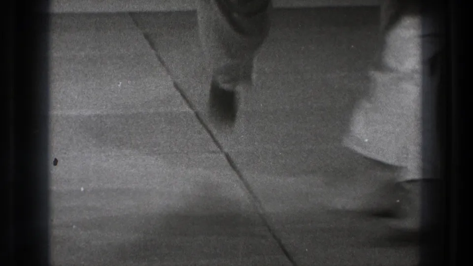 Soft black-and-white 8mm frame from the Tokyo 1971 clip showing blurred movement of karate practitioners on a mat.