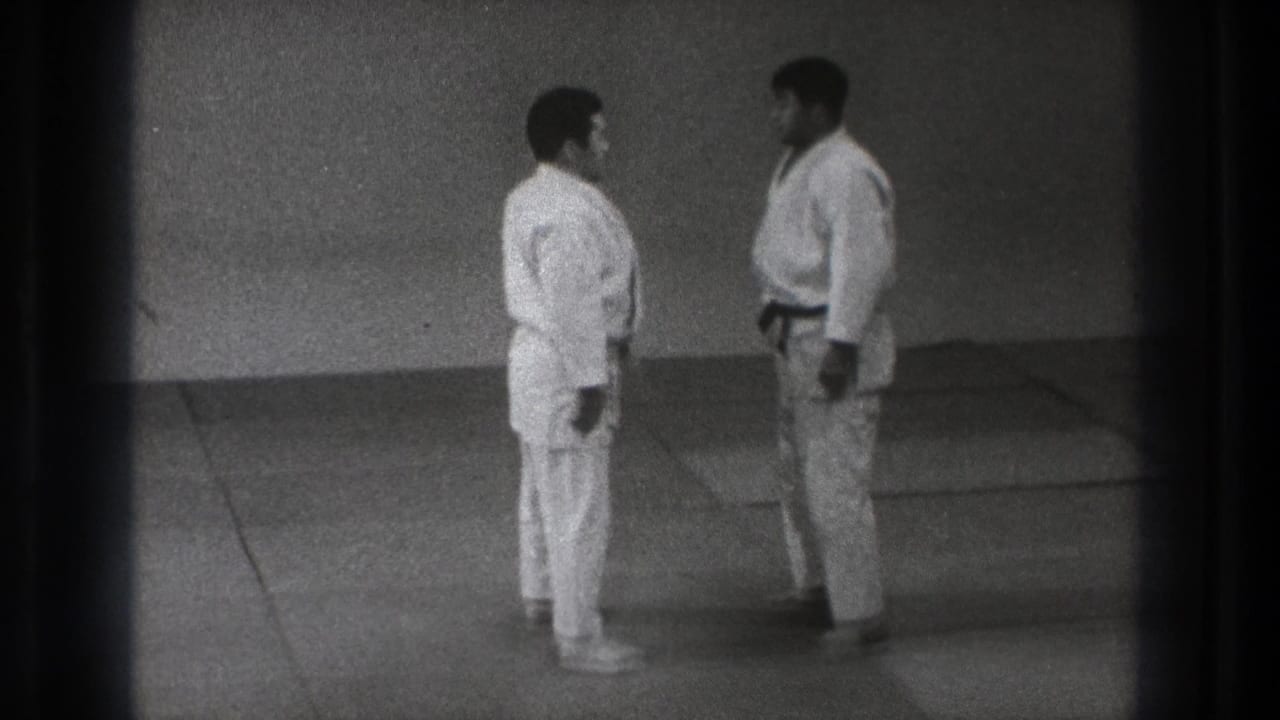 Two adult karate practitioners stand facing each other on a mat in the metadata-supported Tokyo 1971 home-movie footage.