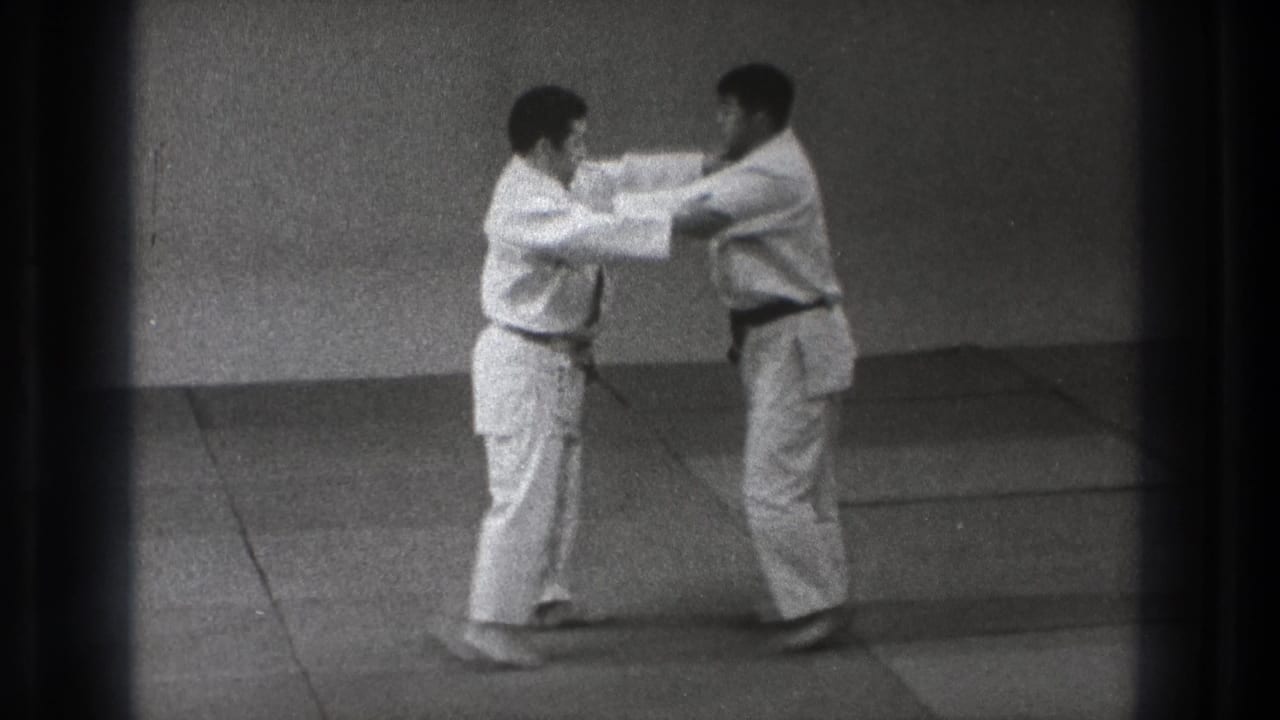 Two adult karate practitioners in white gi make controlled arm contact during a defense-to-attack demonstration in Tokyo 1971 footage.