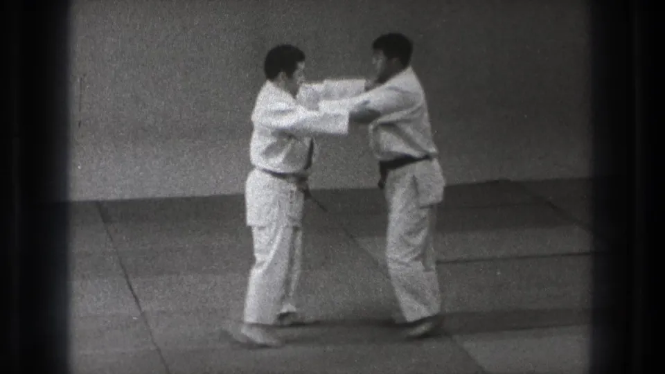 Two adult karate practitioners in white gi make controlled arm contact during a defense-to-attack demonstration in Tokyo 1971 footage.