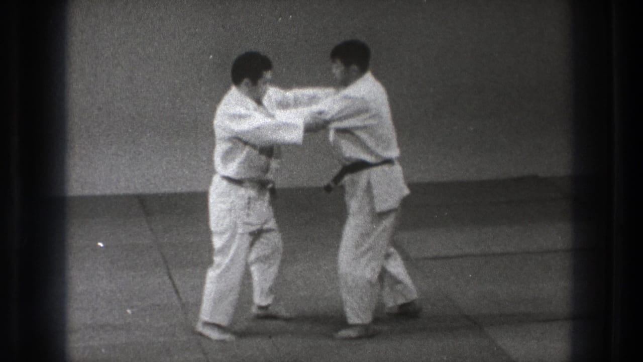 Two men in white gi face each other on a mat with hands gripping near the sleeves.