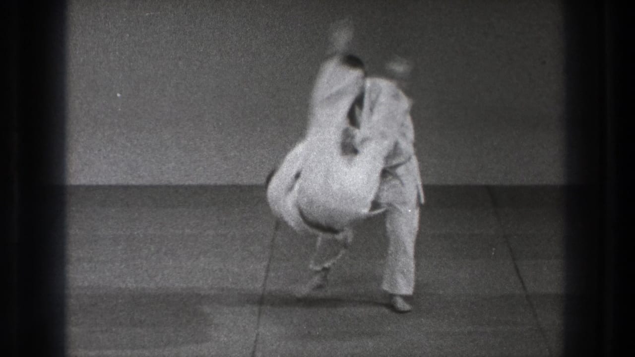 1971 Tokyo 8mm frame of a white-gi practitioner being flipped over during a martial arts throw in a simple indoor practice room.