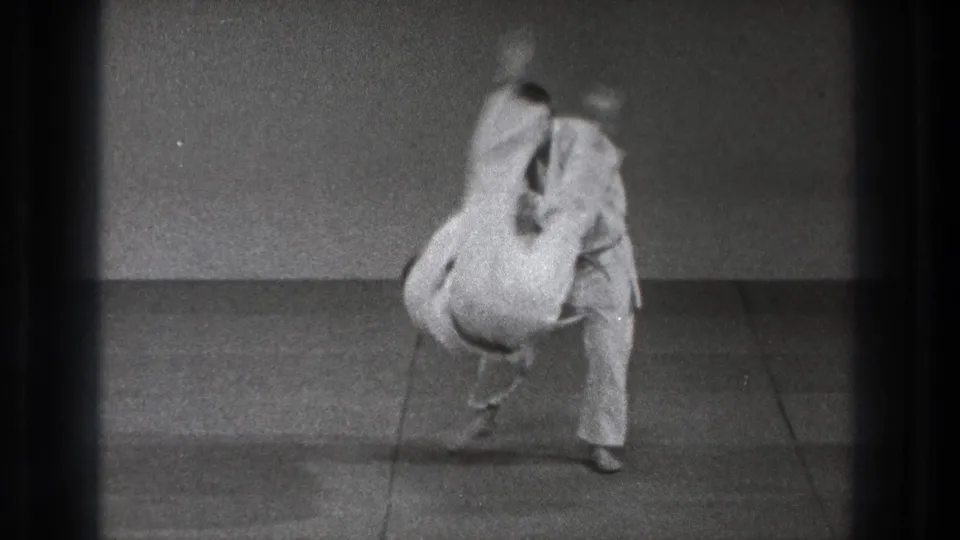 1971 Tokyo 8mm frame of a white-gi practitioner being flipped over during a martial arts throw in a simple indoor practice room.