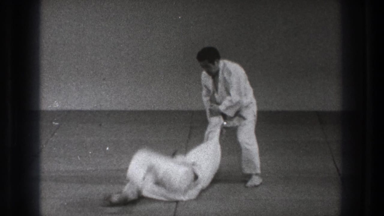 1971 Tokyo 8mm frame showing one martial arts practitioner standing while his partner lands on the indoor mat.