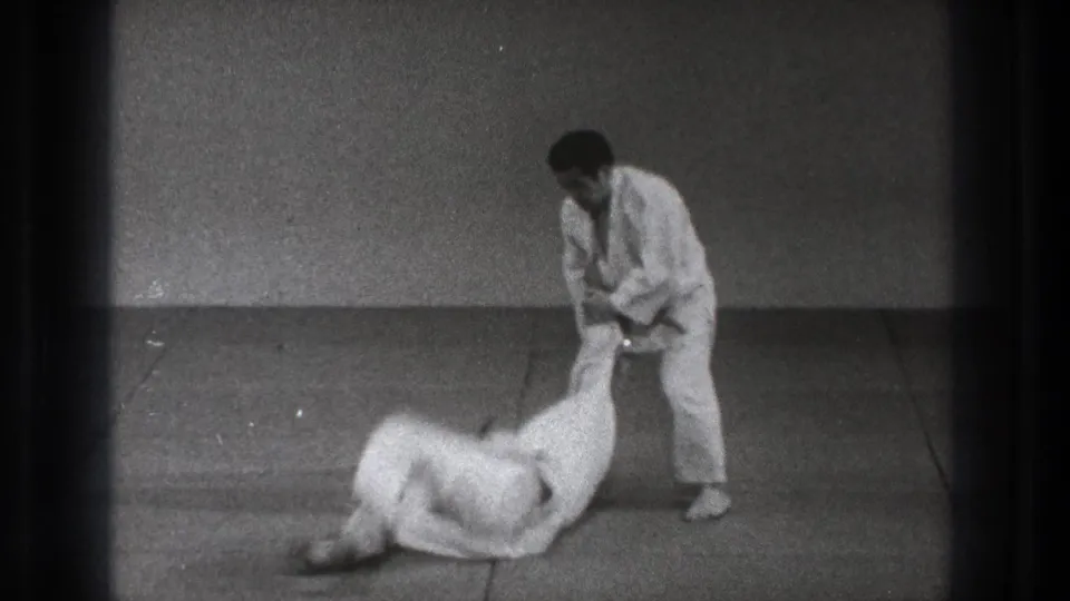 1971 Tokyo 8mm frame showing one martial arts practitioner standing while his partner lands on the indoor mat.
