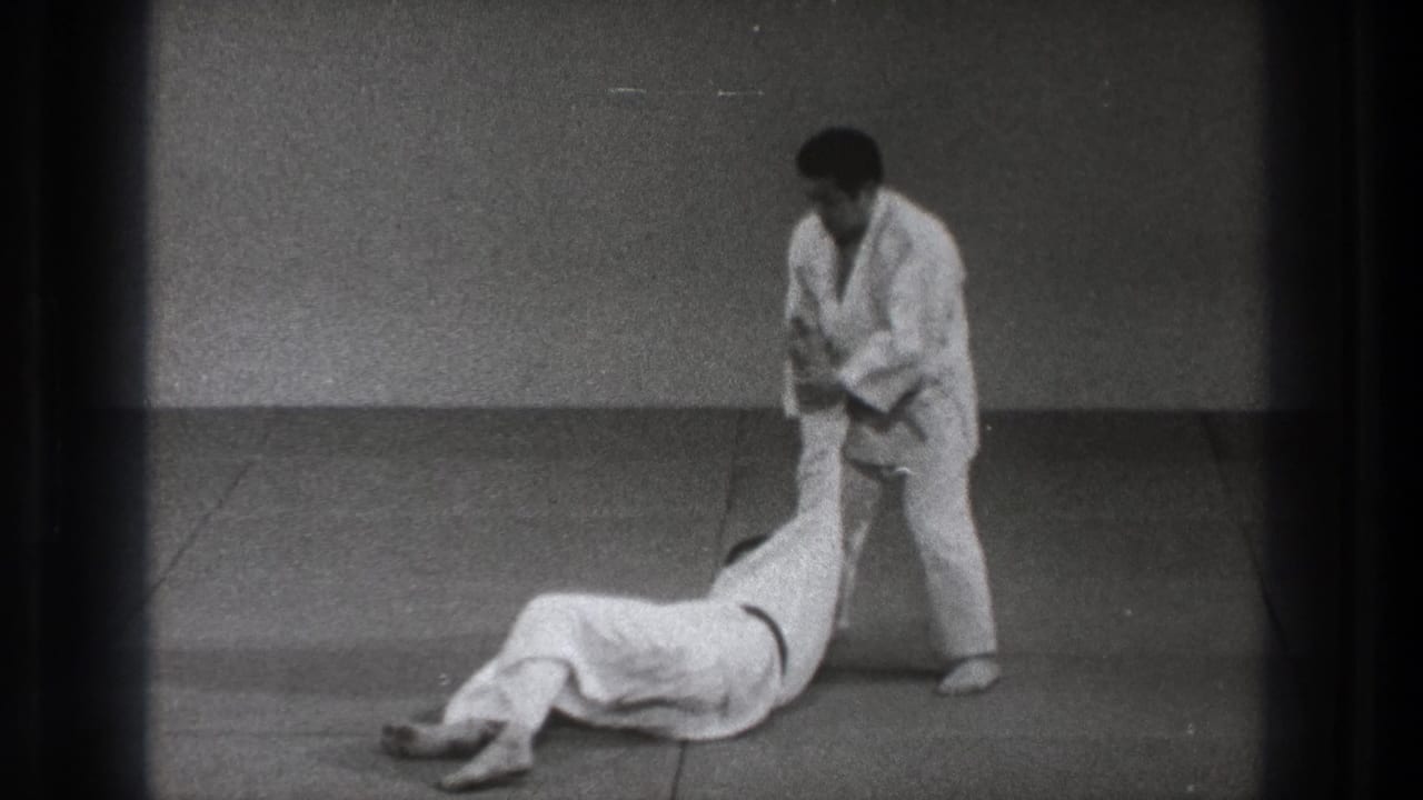 1971 Tokyo 8mm frame of a martial arts throw ending with one practitioner on the mat and the other standing in a white gi.