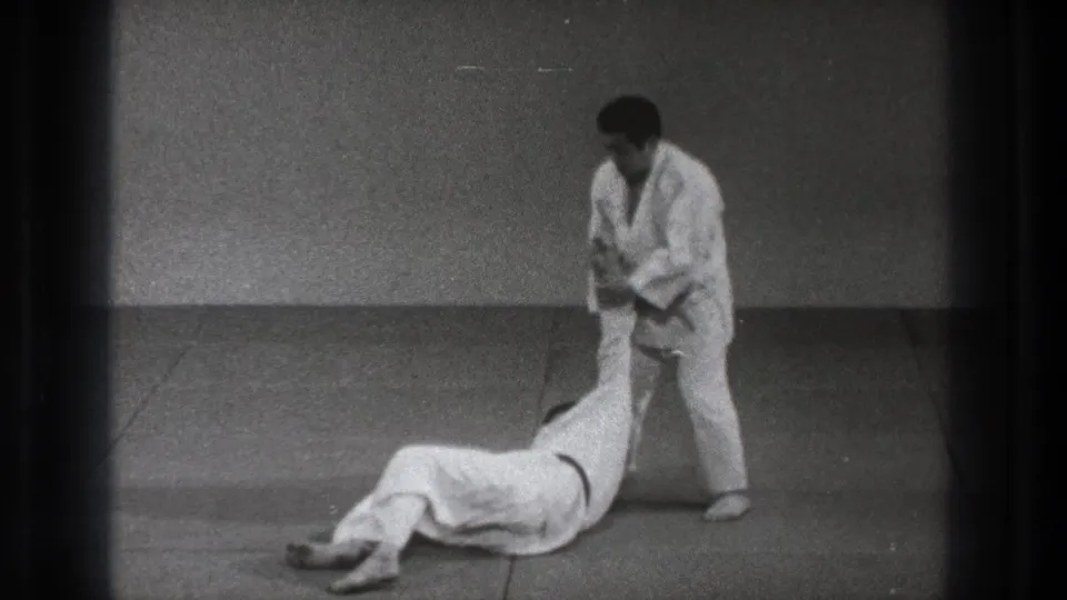 1971 Tokyo 8mm frame of a martial arts throw ending with one practitioner on the mat and the other standing in a white gi.