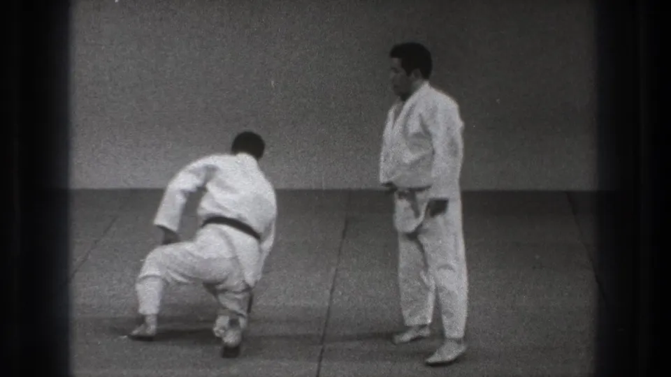 A 1971 Tokyo dojo view shows one adult practitioner pushing up from the mat as his partner in a white gi observes.