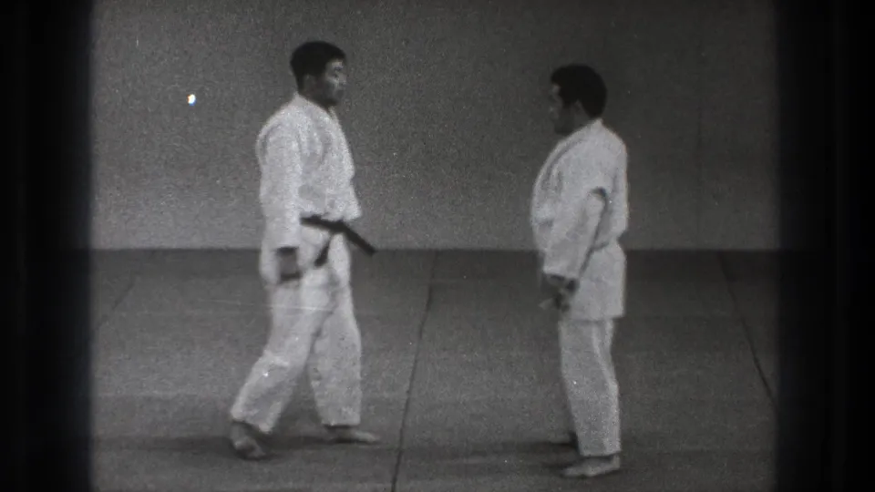 In the final frame, two adult practitioners in white gi stand face to face on mats in the simple 1971 Tokyo dojo scene.