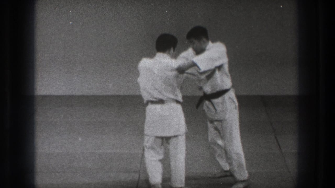 Two men in white gi grip each other on mats during judo practice.