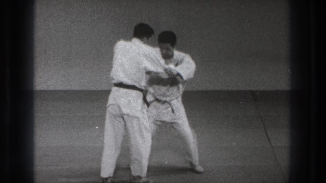 A judo partner turns into position while the other lowers his stance, suggesting setup for a hip throw.