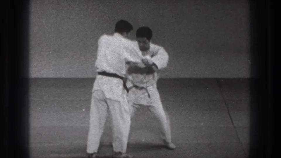 A judo partner turns into position while the other lowers his stance, suggesting setup for a hip throw.