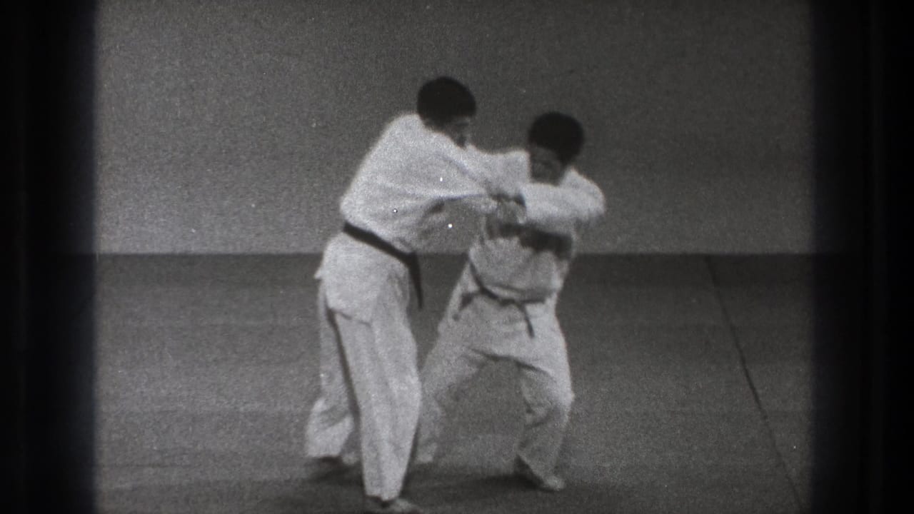In supplied 1971 Tokyo footage, two men in white gi stand on a simple mat as one begins controlling the other's arm and jacket.