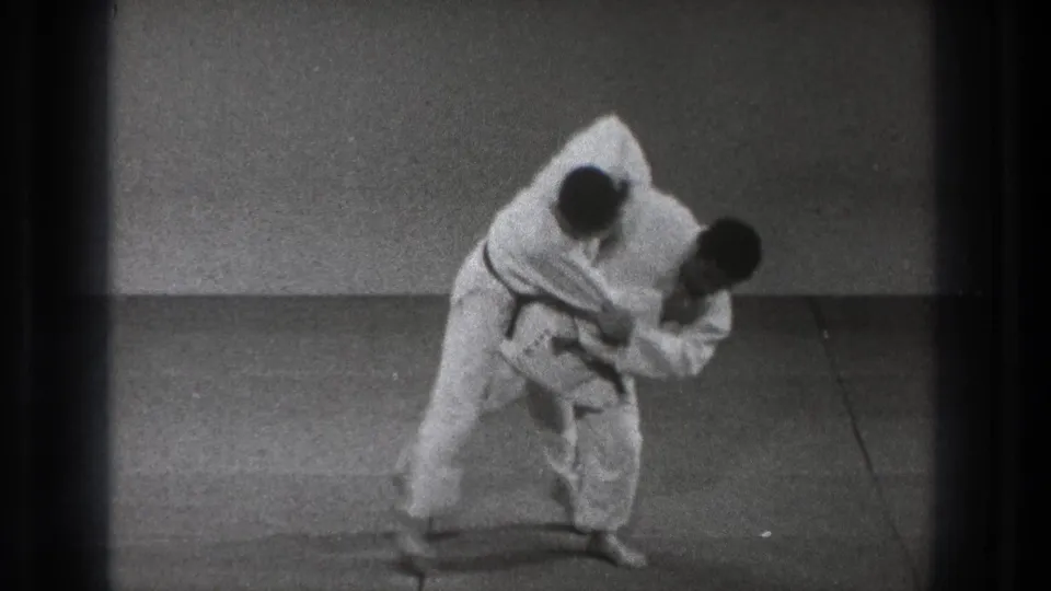 In the Tokyo martial arts scene, the black-belt practitioner turns his body under his partner's grip as the throw begins.